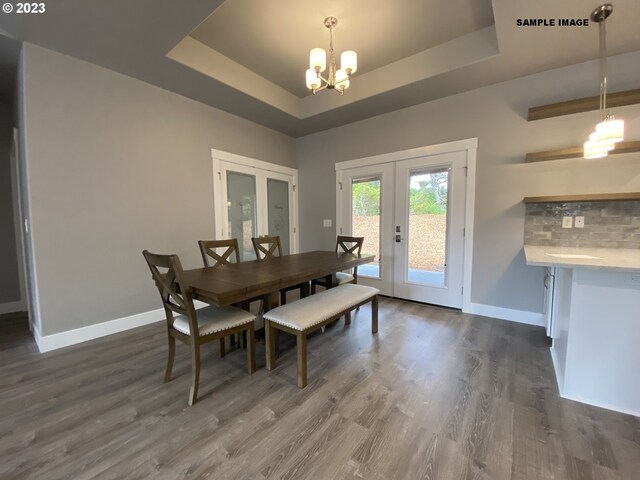 dining space featuring french doors, a notable chandelier, a raised ceiling, and dark hardwood / wood-style flooring