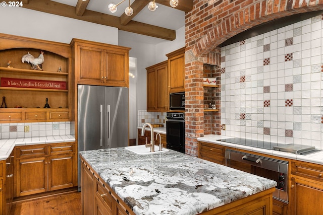 kitchen featuring decorative backsplash, a center island with sink, black appliances, and a sink