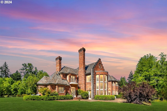 view of front facade with a high end roof, a yard, brick siding, and a chimney