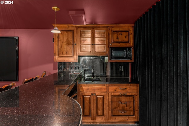 kitchen featuring sink, tasteful backsplash, decorative light fixtures, black microwave, and dark stone counters