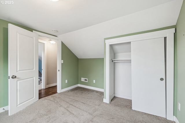 unfurnished bedroom featuring visible vents, lofted ceiling, a closet, carpet floors, and baseboards