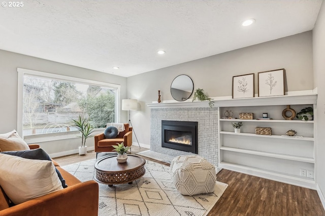 living room with baseboards, a textured ceiling, wood finished floors, and a tile fireplace