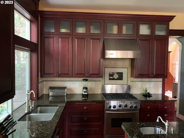 kitchen featuring dark stone countertops, wall chimney range hood, sink, and stainless steel range