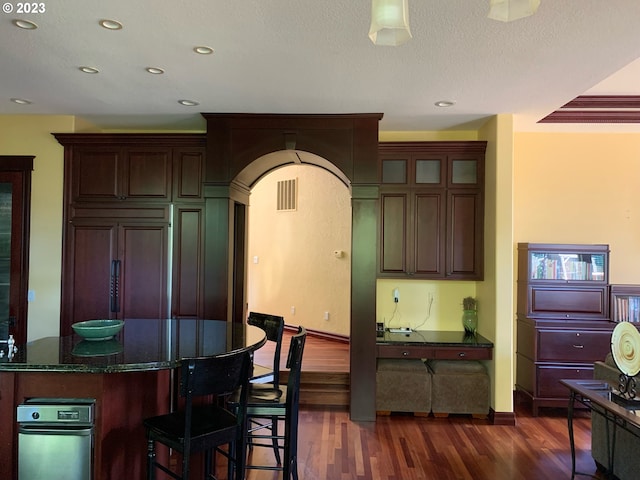 kitchen with a kitchen island, paneled refrigerator, dark stone countertops, a textured ceiling, and dark hardwood / wood-style flooring