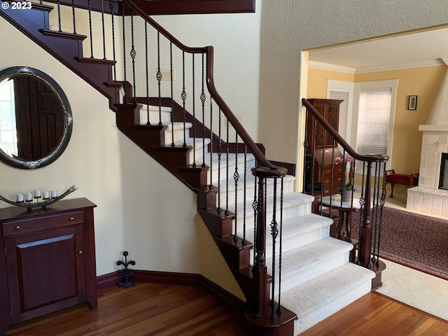 stairs featuring crown molding, hardwood / wood-style floors, and a tiled fireplace