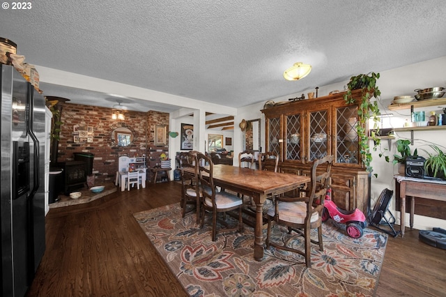 dining room with brick wall, a textured ceiling, a wood stove, and dark hardwood / wood-style floors