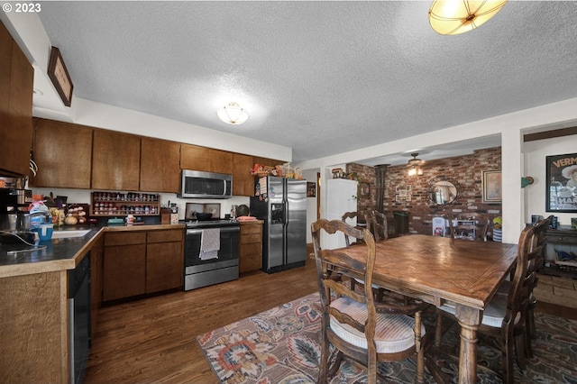 kitchen featuring dark wood-type flooring, brick wall, stainless steel appliances, ceiling fan, and a textured ceiling