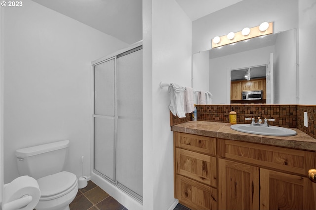 bathroom featuring tile floors, tasteful backsplash, a shower with shower door, toilet, and vanity with extensive cabinet space