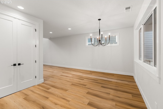 empty room with light hardwood / wood-style flooring and an inviting chandelier