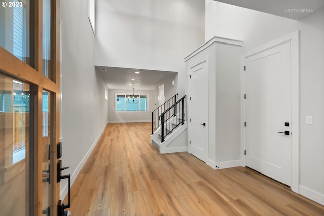 entrance foyer with a notable chandelier, light hardwood / wood-style floors, and a towering ceiling