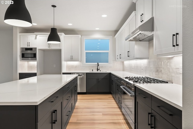 kitchen with white cabinetry, hanging light fixtures, backsplash, appliances with stainless steel finishes, and light hardwood / wood-style flooring