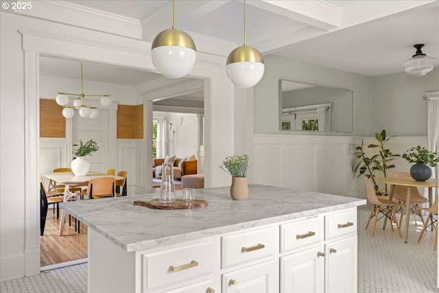 kitchen featuring white cabinetry, light stone counters, wainscoting, and a decorative wall