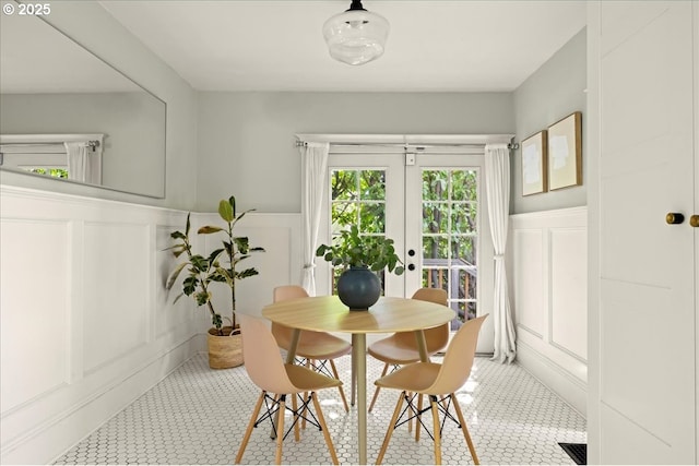 tiled dining area featuring french doors, wainscoting, and a decorative wall