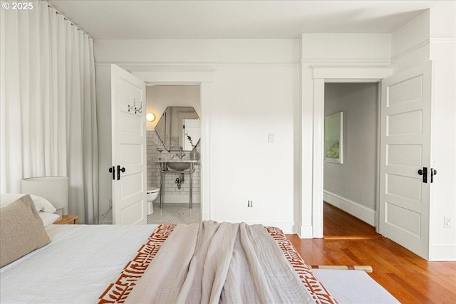 bedroom with baseboards, light wood-type flooring, and connected bathroom