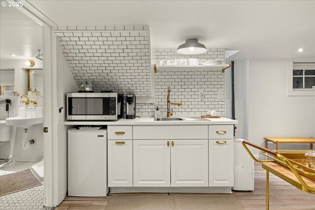kitchen featuring fridge, light wood-type flooring, stainless steel microwave, white cabinets, and a sink