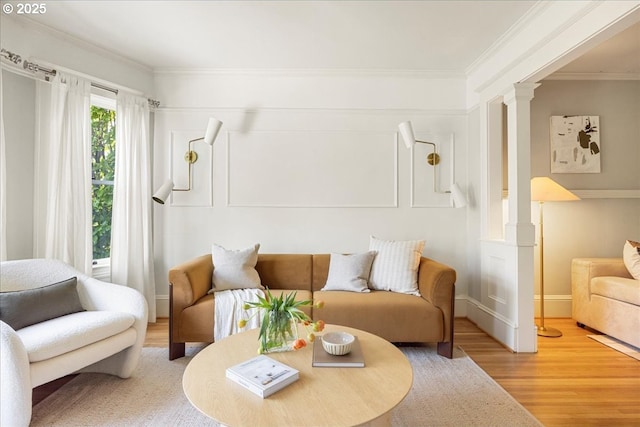 living room with crown molding, ornate columns, baseboards, and light wood finished floors
