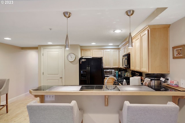 kitchen featuring decorative light fixtures, a kitchen breakfast bar, kitchen peninsula, light hardwood / wood-style flooring, and black appliances