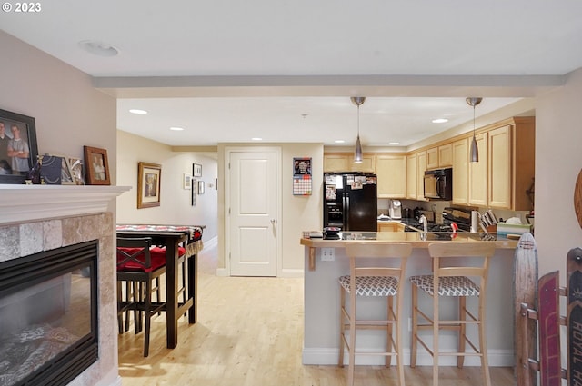 kitchen featuring a tiled fireplace, decorative light fixtures, light hardwood / wood-style floors, and black appliances