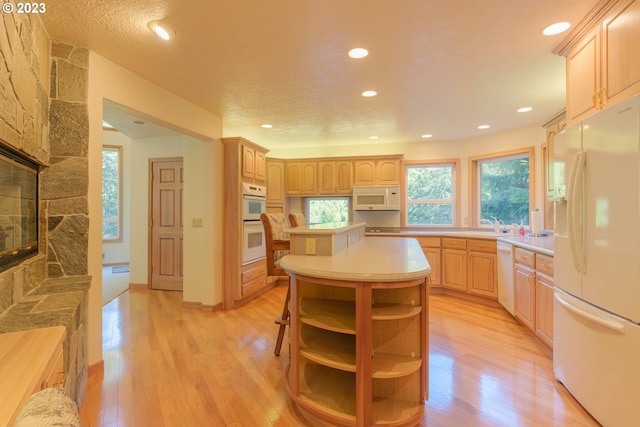 kitchen featuring white appliances, a kitchen island, light hardwood / wood-style flooring, a fireplace, and light brown cabinets