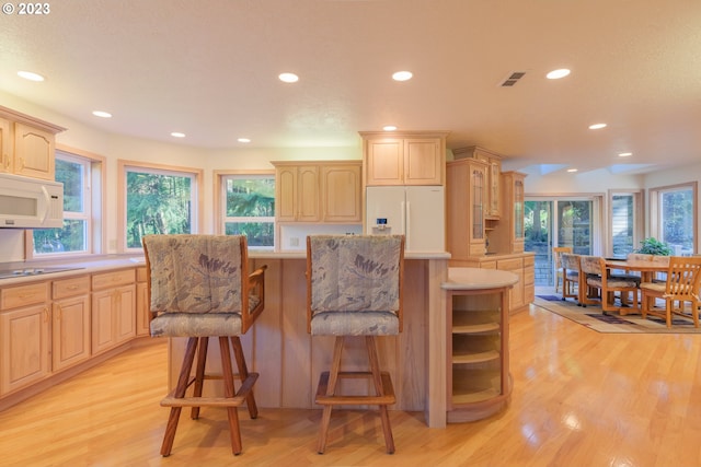 kitchen featuring white appliances, light brown cabinets, light hardwood / wood-style floors, and a breakfast bar area