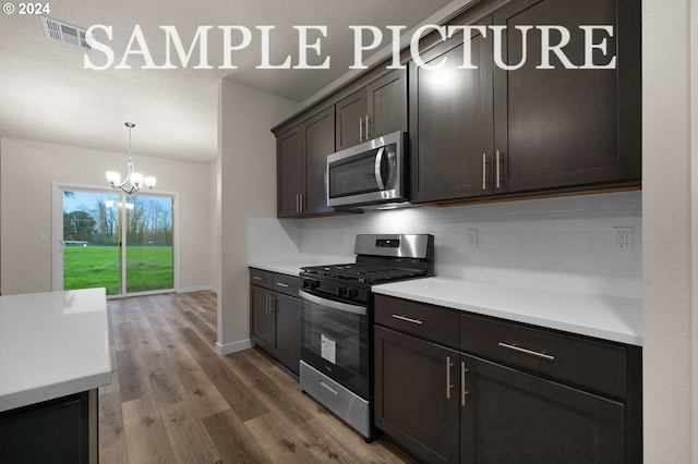 kitchen featuring appliances with stainless steel finishes, tasteful backsplash, dark brown cabinets, an inviting chandelier, and hardwood / wood-style floors