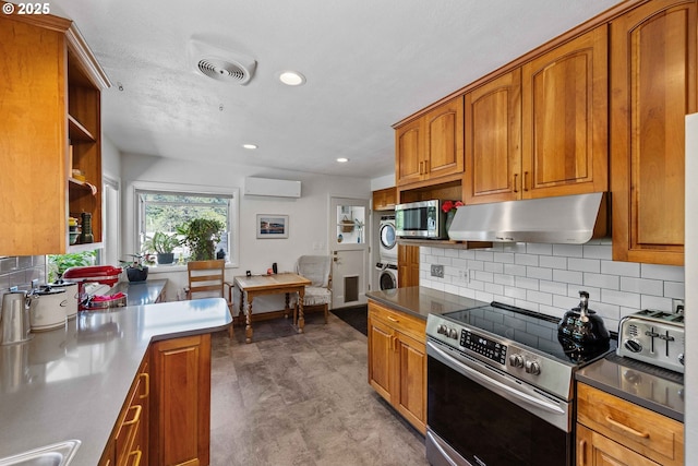 kitchen featuring brown cabinets, under cabinet range hood, stacked washer / dryer, and stainless steel appliances