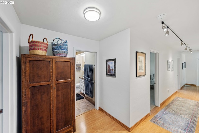 hallway with track lighting, baseboards, and light wood finished floors
