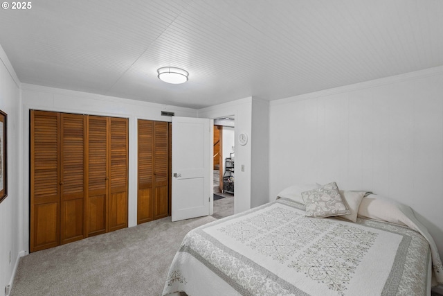 bedroom featuring carpet floors, ornamental molding, two closets, and visible vents