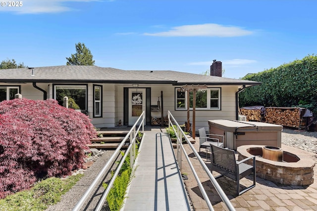 ranch-style home with roof with shingles, a chimney, a hot tub, and a patio area