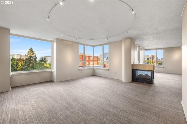 unfurnished living room featuring track lighting, a multi sided fireplace, a textured ceiling, and light colored carpet