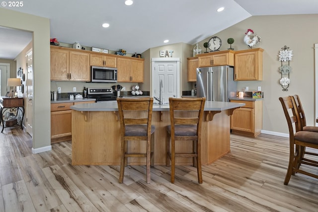 2057 SE Blue Skies Ln, Prineville, OR 97754 - kitchen featuring appliances with stainless steel finishes, lofted ceiling, a kitchen island with sink, light wood-style floors, and a kitchen bar