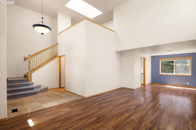 unfurnished living room featuring a skylight, wood finished floors, a towering ceiling, stairway, and baseboards
