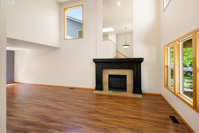 unfurnished living room with a high ceiling, wood finished floors, baseboards, and a fireplace