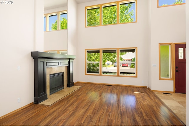 unfurnished living room with a high ceiling, a tiled fireplace, wood finished floors, and baseboards
