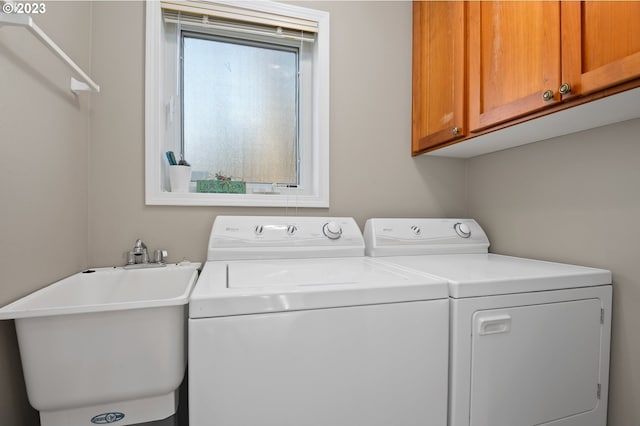 clothes washing area with washing machine and clothes dryer, cabinets, and sink