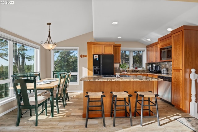 kitchen with light stone counters, stainless steel appliances, light hardwood / wood-style floors, vaulted ceiling, and a wealth of natural light