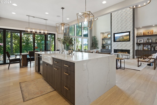 kitchen with a spacious island, pendant lighting, a large fireplace, sink, and light wood-type flooring