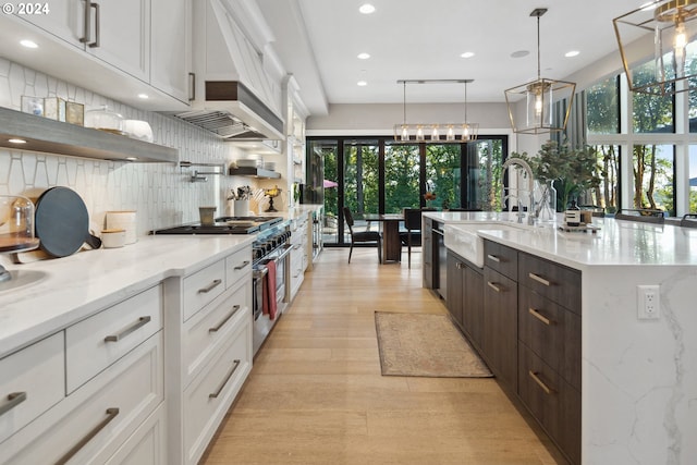 kitchen with hanging light fixtures, white cabinets, sink, and light hardwood / wood-style flooring