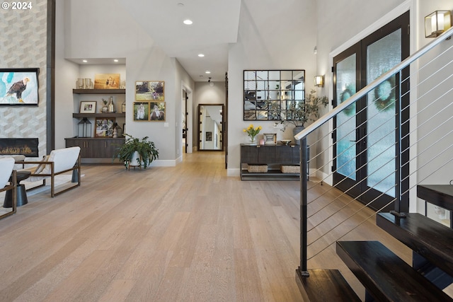 entrance foyer with light hardwood / wood-style flooring, a towering ceiling, and a tiled fireplace