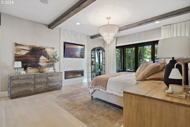 bedroom with light wood-type flooring, a notable chandelier, and a tiled fireplace