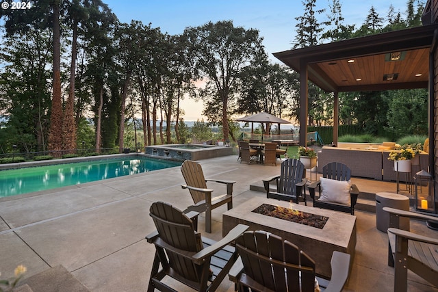 pool at dusk with an outdoor fire pit, a gazebo, a patio area, and an in ground hot tub