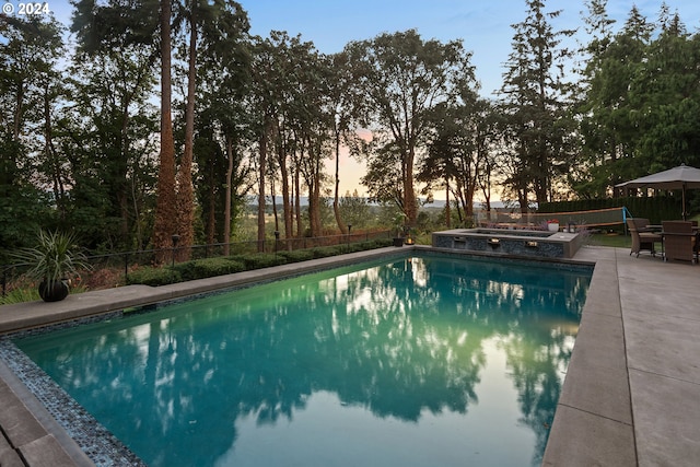 pool at dusk with a patio area and an in ground hot tub