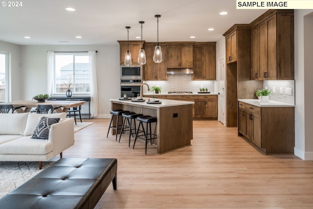 kitchen with a kitchen island with sink, appliances with stainless steel finishes, hanging light fixtures, and light hardwood / wood-style floors