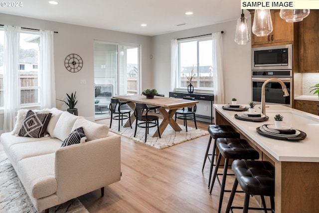 kitchen with appliances with stainless steel finishes, light wood-type flooring, decorative light fixtures, and plenty of natural light