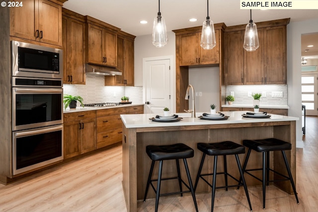 kitchen with hanging light fixtures, light hardwood / wood-style flooring, an island with sink, a breakfast bar area, and stainless steel appliances