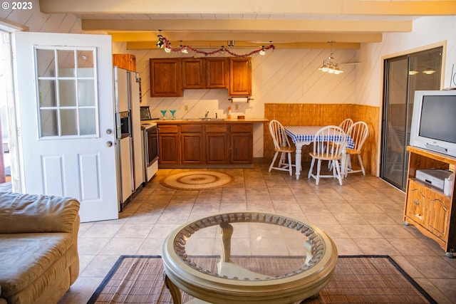 interior space featuring light tile floors, beam ceiling, hanging light fixtures, range, and sink