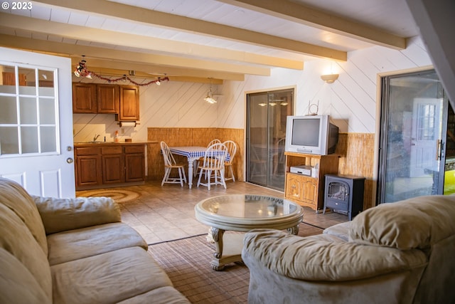 living room featuring a wood stove, sink, beam ceiling, and light tile floors