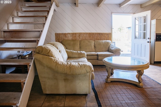 living room with wood walls, dark tile floors, and beam ceiling