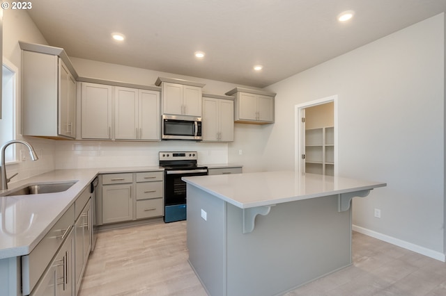 kitchen featuring appliances with stainless steel finishes, light wood-type flooring, a kitchen island, a kitchen breakfast bar, and sink