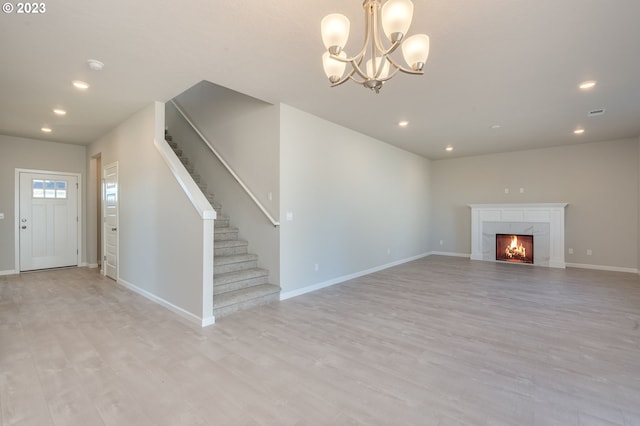 unfurnished living room with a fireplace, a chandelier, and light hardwood / wood-style flooring